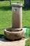 Front view of concrete public water dispenser with shiny metal tap built on top of concrete foundation surrounded with open