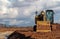 Front view of an excavator, with the lighted empty cabin, between a cloudy sky and the dirt soil