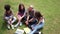 Front view of four college friends sitting on lawn talking.