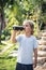 Front view of happy thirsty blond kid boy drinking dark tea from plastic bottle standing outside in summer park nature