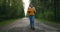 Front view, main plan: a Woman traveling on foot in a yellow sweater and hat on a forest road with a backpack and views