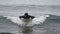 Front view male surfer in wetsuit lying on front on surfboard and rowing hands cruising on breaking wave in Pacific