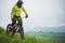 Front view of a man on a mountain bike standing on a rocky terrain and looking down against a gray sky. The concept of a