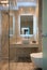 Front view of modern beige marble bathroom with vessel bowl sink, mirror back light, glass shower cabin, wall hung toilet, wooden