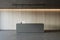 Front view on modern minimalistic reception desk with modern laptop in empty stylish office area, dark lamp on wooden wall