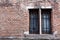 Front view old brick facade two rectangular windows metal protections. Damaged old construction. Painted distressed wall