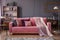 Front view of a pink sofa with pillows and blanket, vintage cupboard in the background in a glamorous living room interior