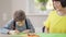 Front view portrait of autistic curios son sitting at table painting as mother talking. Caucasian boy learning at home