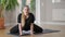 Front view portrait of charming smiling plus-size sportswoman looking at camera breathing in twine pose on exercise mat