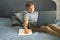 Front view portrait of diligent schoolboy writing or drawing, sitting on grey sofa while doing homework. Studying online during