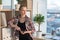 Front view portrait of a female interior designer standing at art studio, leaning on bookshelves, watching aside