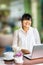 Front view portrait of happy Asian businesswoman sitting at long table in coffee shop and using laptop computer. Freelancer workin