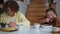 Front view portrait of schoolboy and schoolgirl eating morning cereal sitting at table in living room. Sleepy Caucasian