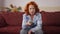 Front view retro woman looking at camera choosing channel switching with remote control. Caucasian redhead lady sitting