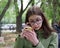 Front view of a sad cute Caucasian girl in blue glasses and a green jacket wiping a tear when looking at the phone