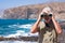 Front view of senior man holding binoculars looking smiling at camera. Senior white haired pensioner enjoying retirement at sea.