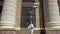 A front view slow motion general shot of a youthful woman going down the stairs between two columns and walking towards