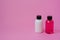 Front view of small white and pink bottles on a pink background. Cosmetics on the road for skin care or hair.