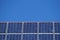 Front view of solar panels on a roof with deep blue cloudless sky in background. Photovoltaic installation of a house in daylight