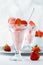 A front view of a strawberry ice cream sundae with another one on a metal tray in behind and a bowl of strawberries.