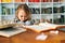 Front view of tearing upset primary child school girl sitting alone hugging knees in front of desk with difficult