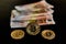 Front view of three Bitcoin coins, next to a group of Euro banknotes, on a black background. Concept of money, power, economics,