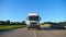 Front view of truck with cargo trailer driving on highway transporting goods at summer day. White lorry riding through