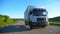 Front view of truck with cargo trailer speeding on highway and transporting goods at sunny day. White lorry riding