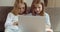 Front view of two little schoolgirls friends sitting together on couch at home in front of laptop screen watching