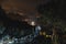 Front view. Two tourists on top of the mountain. Climbing, hiking trail. View of the night city. Romantic setting. Couple in love