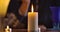 Front view of white candle standing on the table and female Caucasian hand lighting it up. Unrecognizable magician in