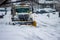 Front view of white snow plow truck with curved yellow blade removing snowfall off roads in suburban area during winter after a