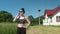 Front view of young brunnette in a green field with rural white house on background talking on phone. Sunny summer