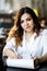 Front view. Young woman sits in cafe at a table, holding pen, reading documents. A businesswoman signs a contract. Startup,