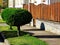 front yard with classic fence along sidewalk. vertical stained brown wood planks. mediterranean type green garden