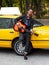 Frontal portrait of cheerful modern multiple race guy in casual clothes near yellow vintage car, play at guitar outside.