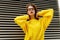 Frontal portrait trendy brown hair girl in eyeglasses, makeup wearing in yellow sweater in the city. Horizontal view.
