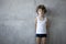 Frontal portrait of a unhappy curly little boy in underwear poses on concrete wall, copy space