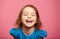 Frontal shot of laughter joyful little girl stands beside pink wall.