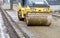 Frontal view of a road roller rolling the base of the sidewalk along a concrete curb near the carriageway