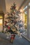 A frosted artificial christmas tree with decorations and fairy lights in front of patio doors during the start of a sunset