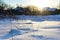 frosty winter morning in countryside. Sun peeks out from behind roofs of houses. Everything is covered with snow