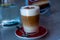 Frothed cappuccino with spoon on a table water and cake in background