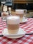 Frothy, layered cappuccino in a clear glass mug. Tempting coffee latte in two tall glasses in coffee house. Cafe and bar