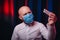 Frowned man in gauze mask and white shirt holding medicines in hand on dark background. Emotion of doubt and fear. Healthcare