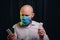 Frowned man in gauze mask and white shirt holding medicines in hands on dark background. Healthcare, respiratory illness preventio