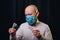 Frowned man in gauze mask and white shirt holding medicines in hands on dark background. Healthcare, respiratory illness preventio