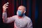 Frowned man in gauze mask and white shirt holding medicines in hands on dark background. Prophylaxis of virus infections, COVID-19