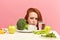 Frowning woman dislikes vegetables on table with disgusting grimace isolated