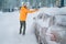 Frozen automobile on the countryside forest home driveway with man removing snow from car roof using big snow brush on the